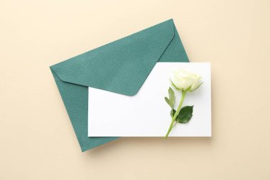 Boş davetiye kartı, bej arka planda zarf ve çiçek, üst görünüm