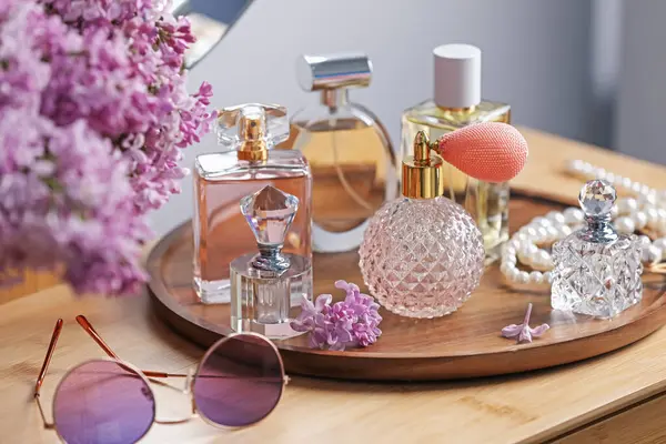 Parfüm şişeleri, aksesuarlar ve ahşap masada leylak çiçekleri.