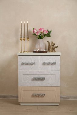 Mumları yanan zarif şamdanlar vazoda laleler ve bej duvarın yanındaki şifoniyerde diğer dekorlar.