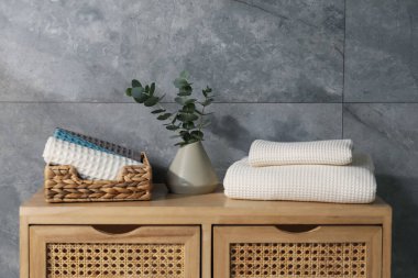 Gri duvarın yanındaki ahşap şifoniyerde dalları olan gözleme havluları ve vazolar.