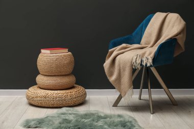 Bej renkli yün battaniyeli rahat bir koltuk ve gri duvarın yanında kitap.