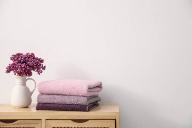 Beyaz duvarın yanındaki ahşap dolapta, yumuşak havlular ve leylak çiçekleri yığını.