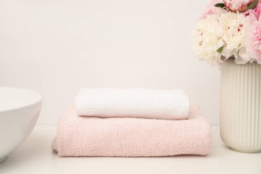Beyaz tezgahta yumuşak havlular ve şakayık çiçekleri, yakın plan.