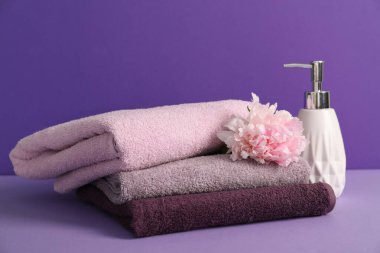 Yumuşak havlu yığını, şakayık çiçeği ve mor arka planda sıvı sabun.