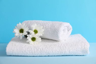 Açık mavi arka planda yumuşak havlular ve kasımpatı çiçekleri