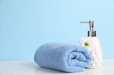 Yumuşak havlu, sıvı sabun ve kasımpatı çiçeği açık mavi arkaplanda, metin için boşluk