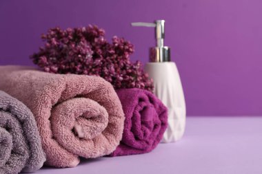 Yumuşak havlular, sıvı sabun ve mor arka planda leylak çiçekleri, yakın plan. Metin için boşluk