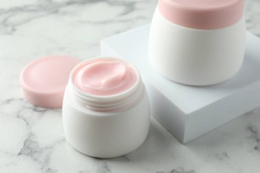 Kavanozlar dolusu nemlendirici vücut kremi beyaz mermer masada, yakın plan.