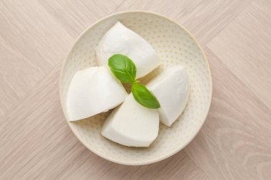 Lezzetli mozzarella peyniri ve fesleğen parçaları ahşap masada, üst tarafta.