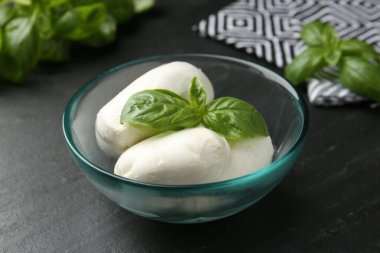 Lezzetli mozzarella peyniri ve fesleğen parçaları koyu dokulu masada, yakın plan.