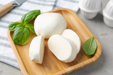 Lezzetli mozzarella peyniri ve fesleğen yaprakları. Gri desenli masa, yakın plan.