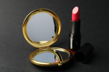 Siyah arkaplanda cep aynası ve ruj, yakın plan.