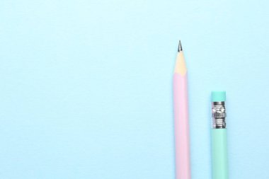 Açık mavi arka planda iki grafit kalem, düz. Metin için boşluk