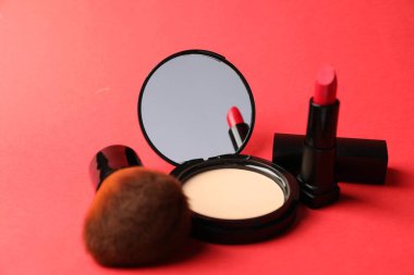 Aynalı yüz pudrası, kırmızı arka planda ruj ve fırça, yakın plan