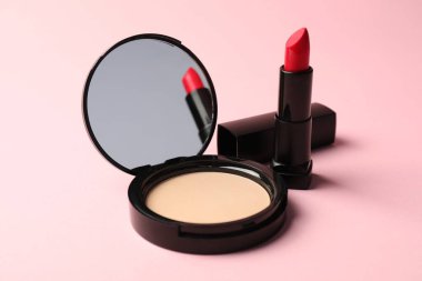 Aynalı açık yüz pudrası ve pembe arka planda ruj, yakın plan.