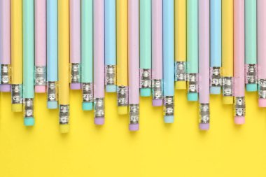 Sarı arka planda silgisi olan bir sürü grafit kalem, düz bir zemin. Metin için boşluk