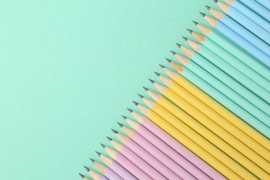 Turkuaz arka planda bir sürü grafit kalem, düz bir zemin. Metin için boşluk