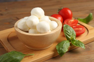 Lezzetli mozarella topları, domatesler ve fesleğenler ahşap masada, yakın plan.