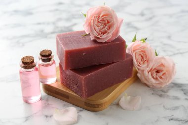 Sabun barları, kozmetik ürünleri ve beyaz mermer masada güzel güller, yakın plan.