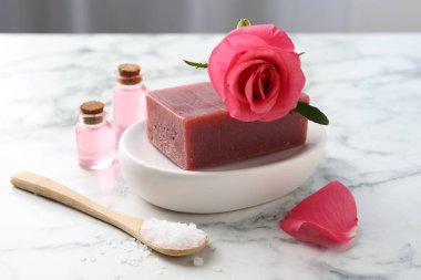 Sabun barları, kozmetik ürünleri ve beyaz mermer masada güzel bir gül.