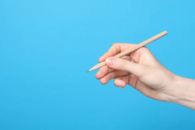 Açık mavi arka planda grafit kalemi olan kadın, yakın plan. Metin için boşluk