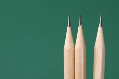 Yeşil arka planda üç grafit kalem, yakın plan. Metin için boşluk