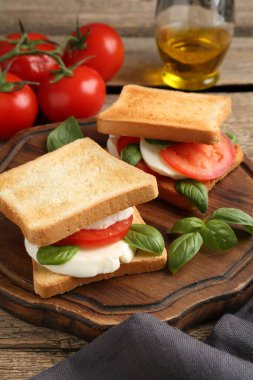 Mozarella peynirli, domatesli ve ahşap masadaki fesleğenli lezzetli sandviçler.