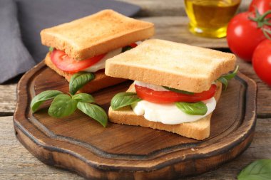 Mozarella peynirli, domatesli ve ahşap masadaki fesleğenli lezzetli sandviçler.