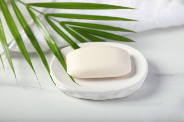 Sabun çubuğu, havlu ve palmiye yaprağı beyaz mermer masada, yakın plan.