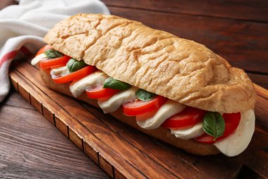 Mozarella peynirli, domatesli ve ahşap masadaki fesleğenli lezzetli sandviç.