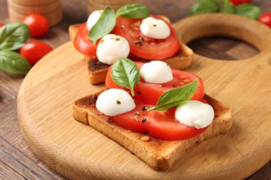 Mozarella peynirli, domatesli ve ahşap masadaki fesleğenli lezzetli sandviçler.