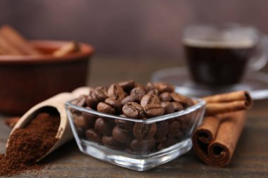 Kavrulmuş fasulye, hazır kahve tozu ve tarçın çubukları ahşap masada kahverengi arka planda, yakın plan.