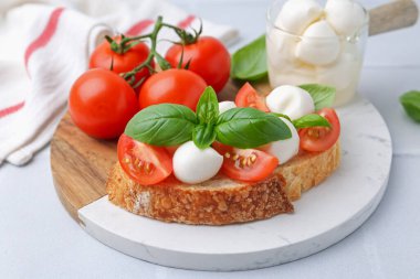 Peynirli lezzetli sandviç, domates ve fesleğen açık gri desenli masa, yakın plan.