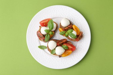 Mozarella peynirli lezzetli sandviçler, yeşil arka planda domates ve fesleğen.