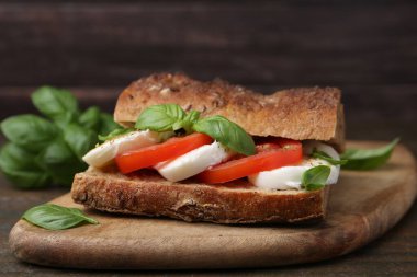 Mozarella peynirli, domatesli ve ahşap masadaki fesleğenli lezzetli sandviç.