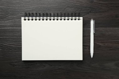 Boş defter ve kalemi siyah ahşap masa üzerinde aç, üst görünüm