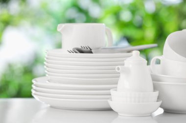 Beyaz masadaki farklı temiz tabaklar, bulanık yeşil arka plan, yakın plan