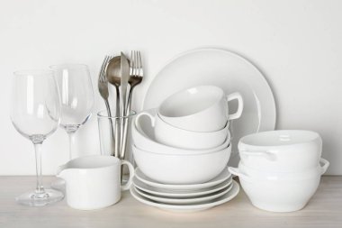 Beyaz duvarın yanındaki açık ahşap masada farklı temiz bulaşık takımı.