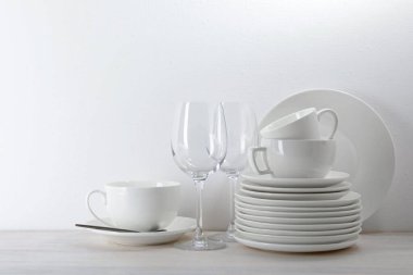 Beyaz duvarın yanındaki açık ahşap masada farklı temiz bulaşık takımı.