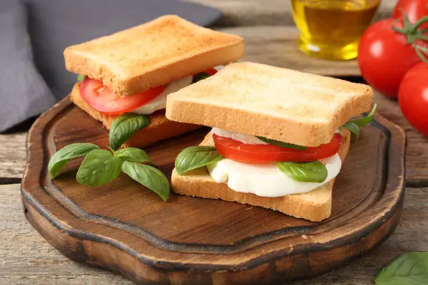 Mozarella peynirli, domatesli ve ahşap masadaki fesleğenli lezzetli sandviçler.