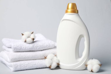 Açık gri arkaplanda bir şişe yumuşatıcı, havlu ve pamuk çiçeği.