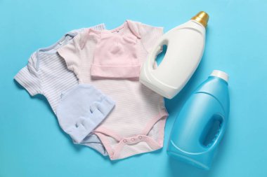 Yumuşatıcı şişeler ve açık mavi arka planda bebek kıyafetleri.