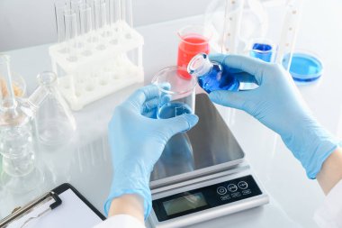 Laboratuvardaki beyaz ayna masasında numune ve terazilerle çalışan bilim adamı.