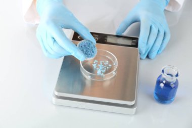 Bilim adamı beyaz ayna masasındaki terazide numune tartıyor, yakın plan.