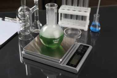 Siyah ayna sehpasında numune ve diğer laboratuvar camlarıyla ölçeklendir, yakın plan.