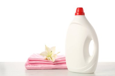 Bir şişe yumuşatıcı, üst üste yığılmış giysiler ve çiçek beyaz arka plana karşı mermer masa