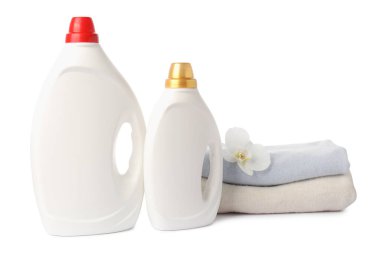 Kumaş yumuşatıcısı şişeleri, üst üste yığılmış giysiler ve beyaz üzerine izole edilmiş çiçekler.