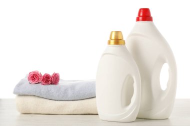 Kumaş yumuşatıcı şişeler, beyaz arka plana karşı ahşap masaya dizilmiş giysiler ve çiçekler.