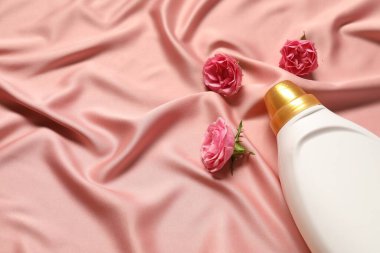 Bir şişe yumuşatıcı ve pembe kumaşlı çiçekler, üst tarafta. Metin için boşluk