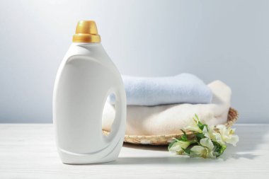 Bir şişe yumuşatıcı, temiz kıyafetler ve beyaz ahşap masa üzerinde zambak çiçekleri.